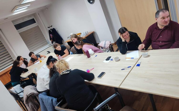 Na zdjęciu widać grupę uczestników siedzących przy dużym, jasnym stole podczas warsztatów. Osoby notują, rozmawiają i aktywnie biorą udział w zajęciach.