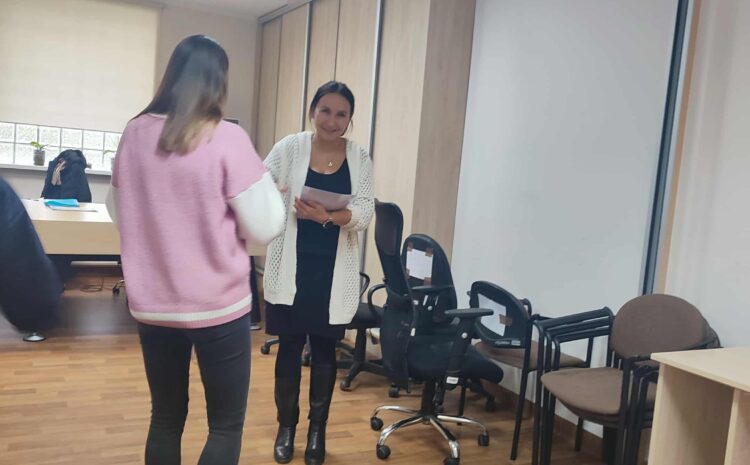 Na zdjęciu uczestniczka podchodzi do prowadzącej, która wręcza jej dyplom. Obi stoją w sali warsztatowej, to moment podsumowania zajęć.